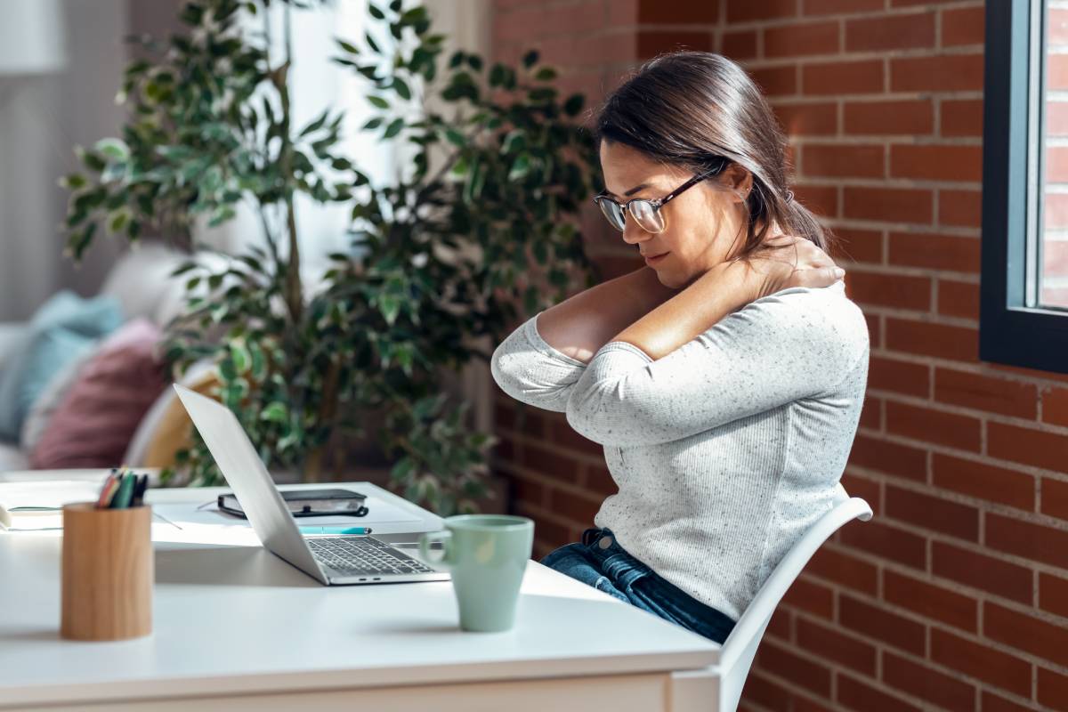Tired business woman with neck pain looking uncomfortable while working with laptop in the office.