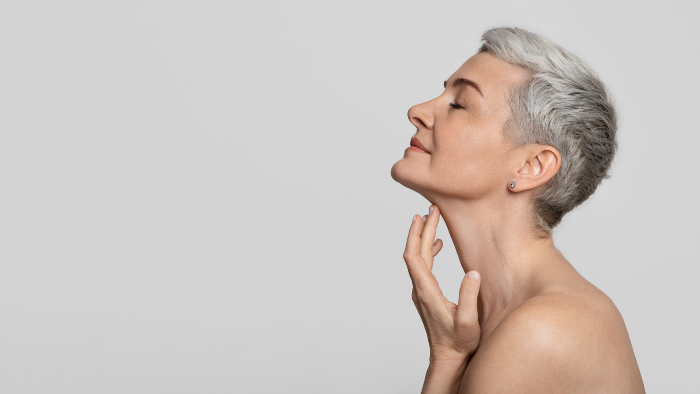 The image shows an older woman touching the smooth skin of her neck. It serves to visually represent how to avoid an artificial-looking neck lift.
